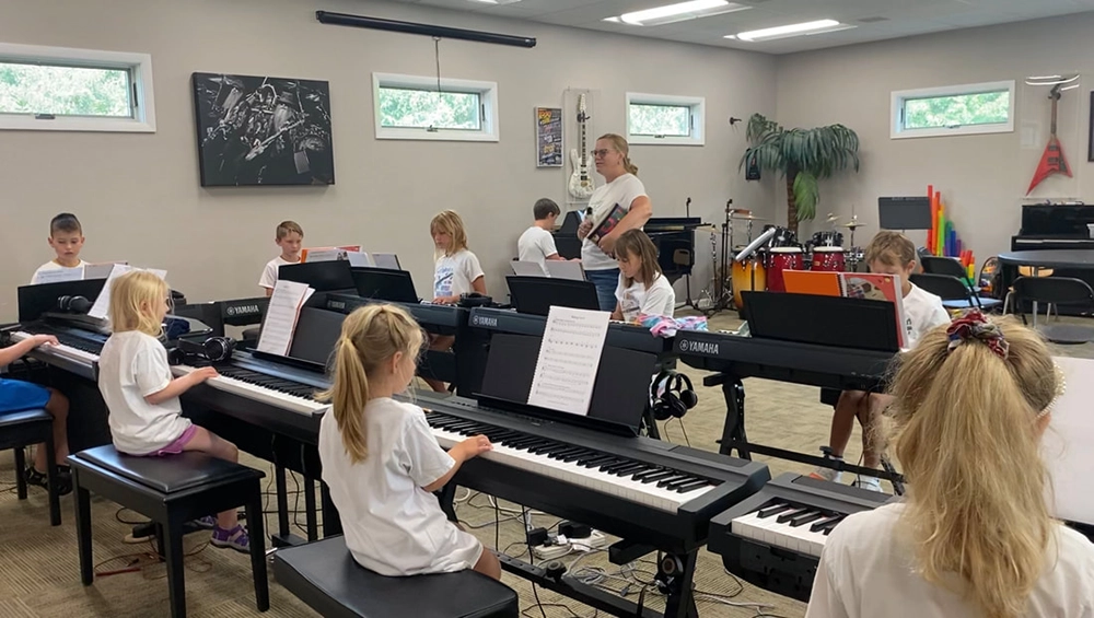 Students listening to a camp instructor in front of their pianos.